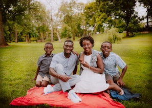 3 women and 2 men sitting on green grass field during daytime