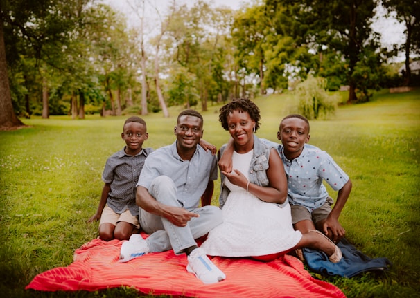 3 women and 2 men sitting on green grass field during daytime