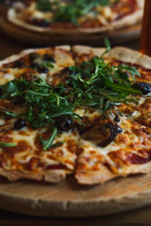 A freshly baked pinsa romana served on rustic wooden table, garnished with fresh toppings.