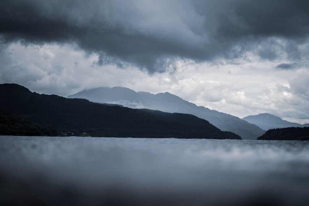 a body of water surrounded by mountains under a cloudy sky