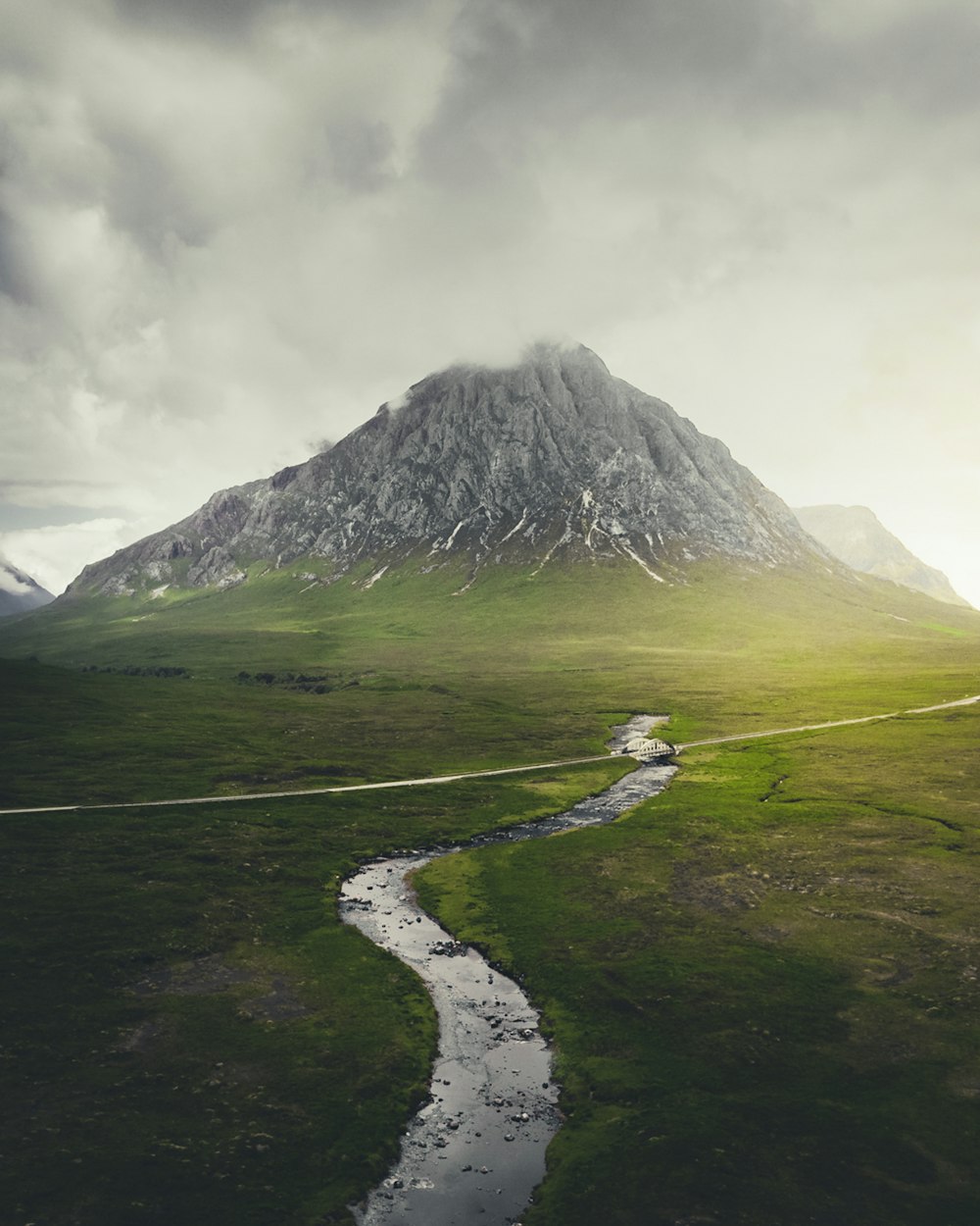 green grass field near mountain under white clouds during daytime