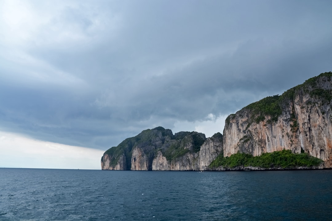 green and brown rock formation on sea under white clouds during daytime