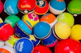 A collection of colorful Pokémon themed balls, each with distinct designs and logos. The balls are tightly packed together, showcasing a variety of vibrant colors and patterns.