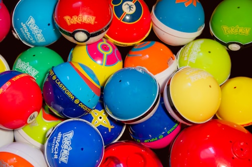A collection of colorful Pokémon themed balls, each with distinct designs and logos. The balls are tightly packed together, showcasing a variety of vibrant colors and patterns.