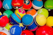 A collection of colorful Pokémon themed balls, each with distinct designs and logos. The balls are tightly packed together, showcasing a variety of vibrant colors and patterns.