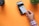 A hand is holding a white credit card near a point-of-sale terminal. The background is an orange surface, and there is a plant and a cup also present in the image.