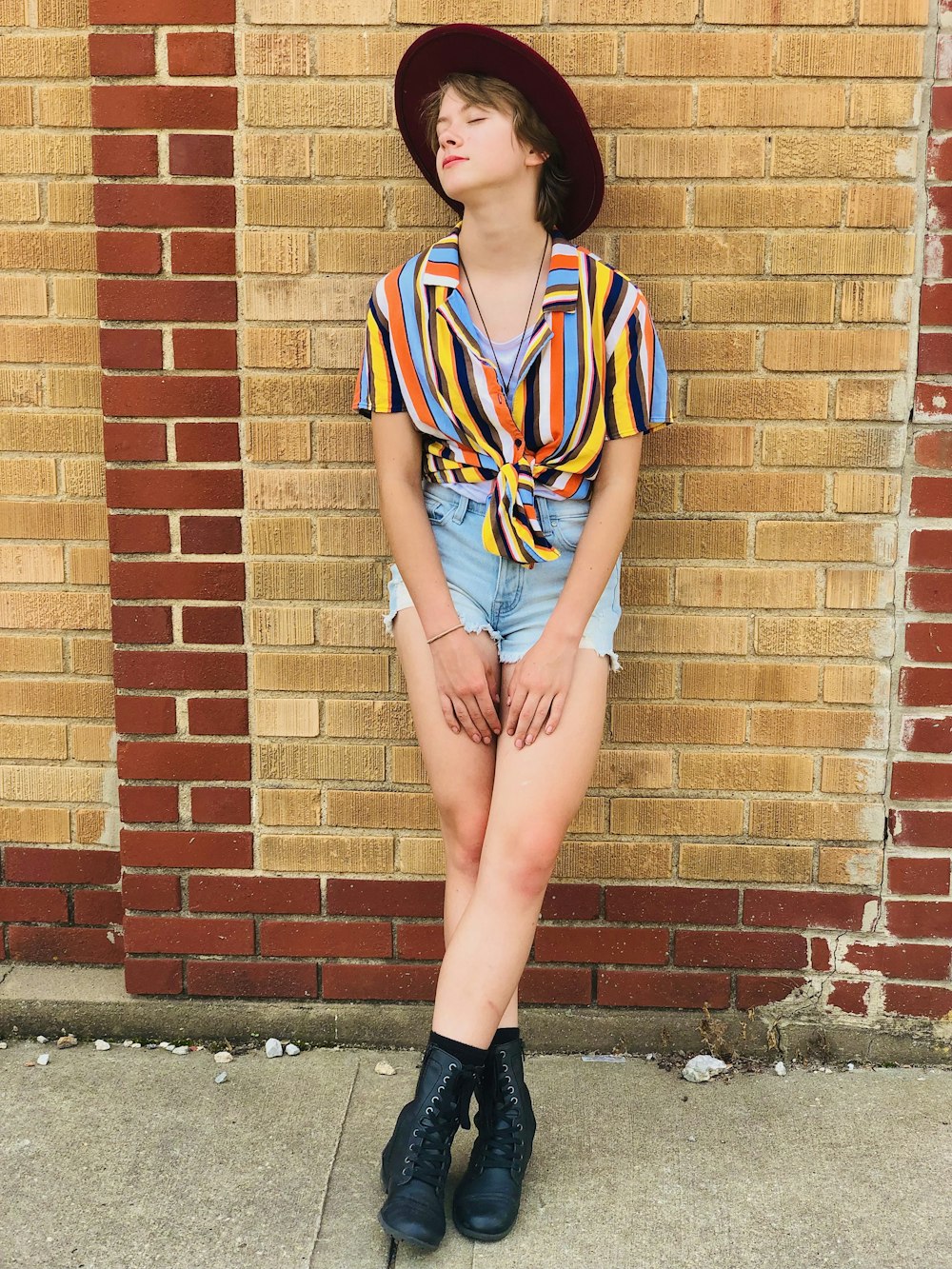 woman in blue red and white stripe shirt and blue denim shorts leaning on brown brick