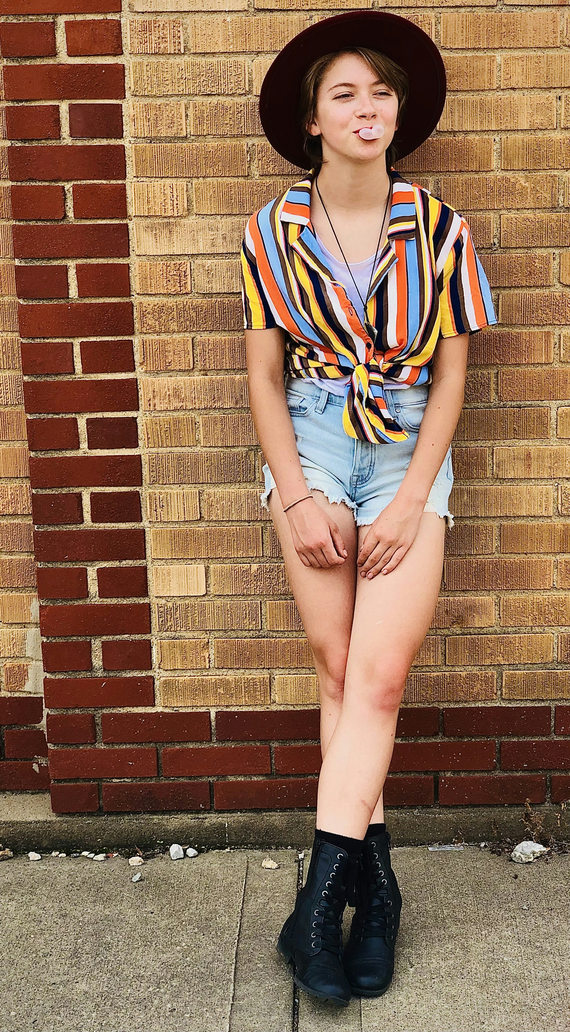 woman in blue denim shorts standing beside brown brick wall