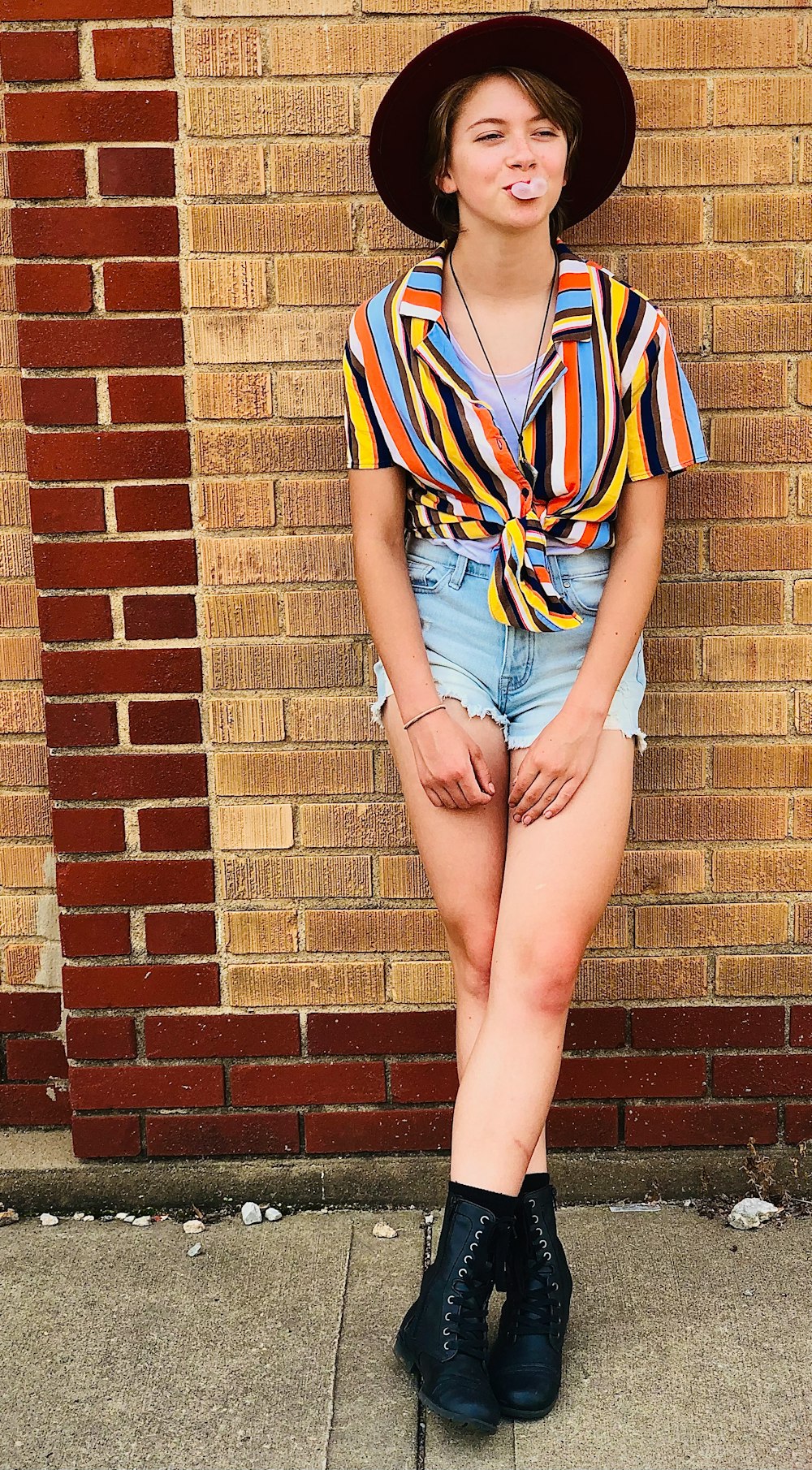 woman in blue denim shorts standing beside brown brick wall