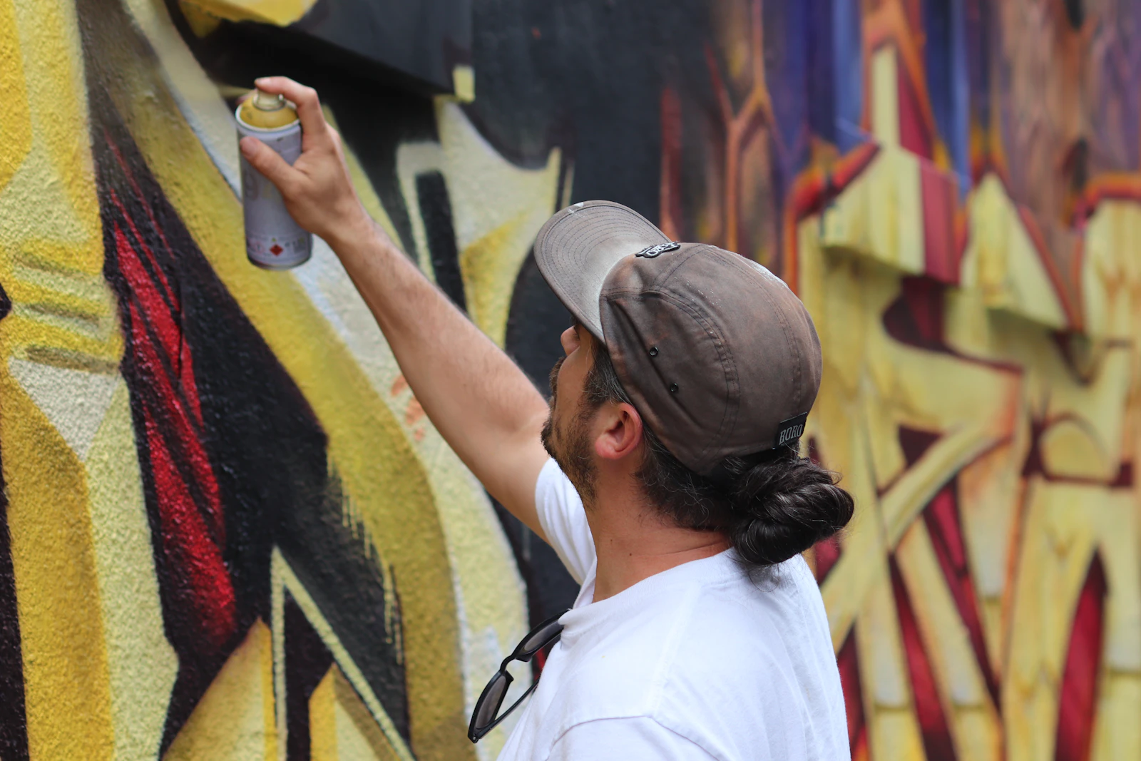 Graffeur peignant une fresque murale à la bombe, le bras levé au-dessus de la ligne des épaules