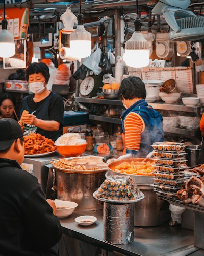 A bustling outdoor food market stall with fresh produce and a vendor cooking to order