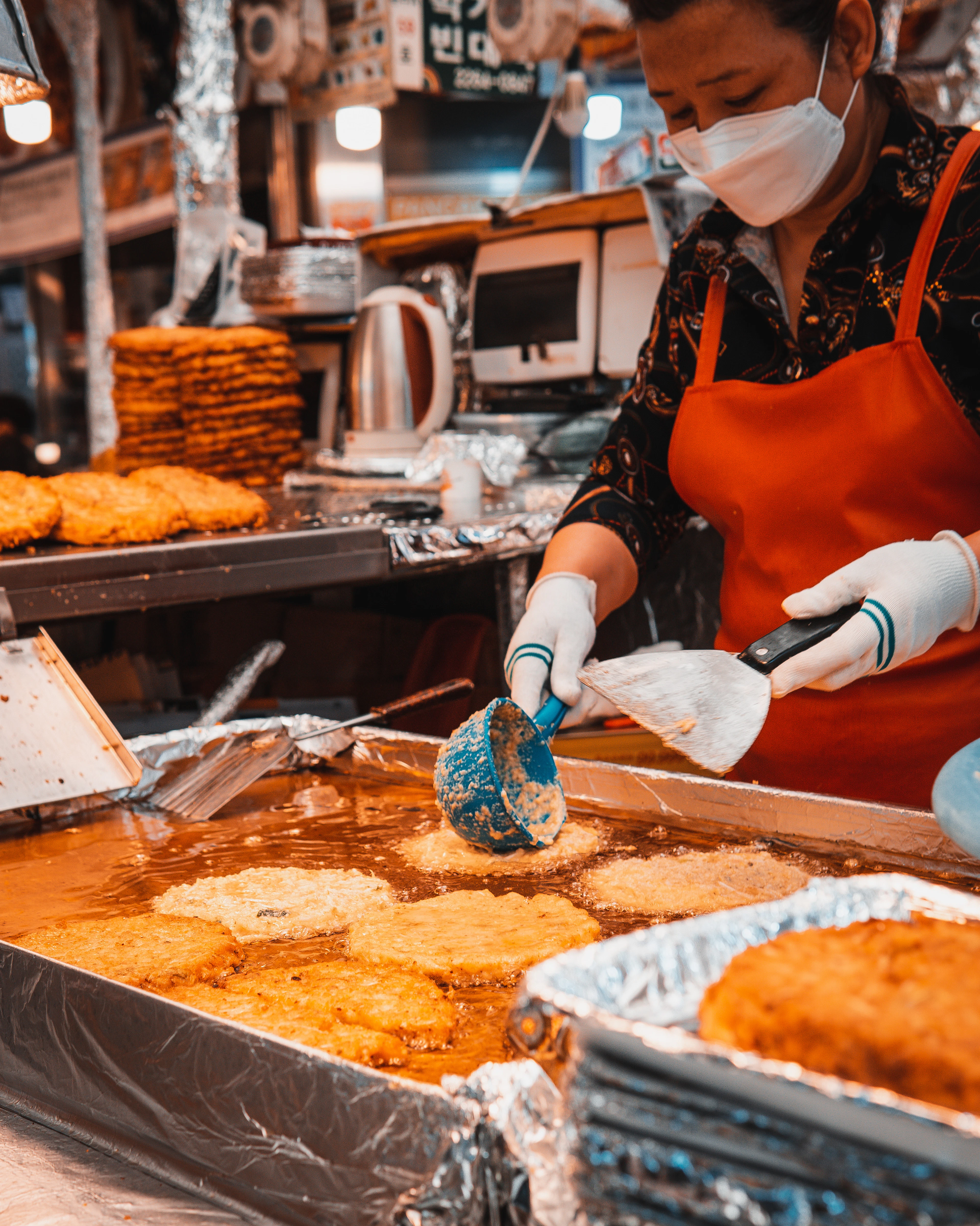 A market vendor fries golden pancakes in a wide pan of bubbling oil at a Seoul food stall.