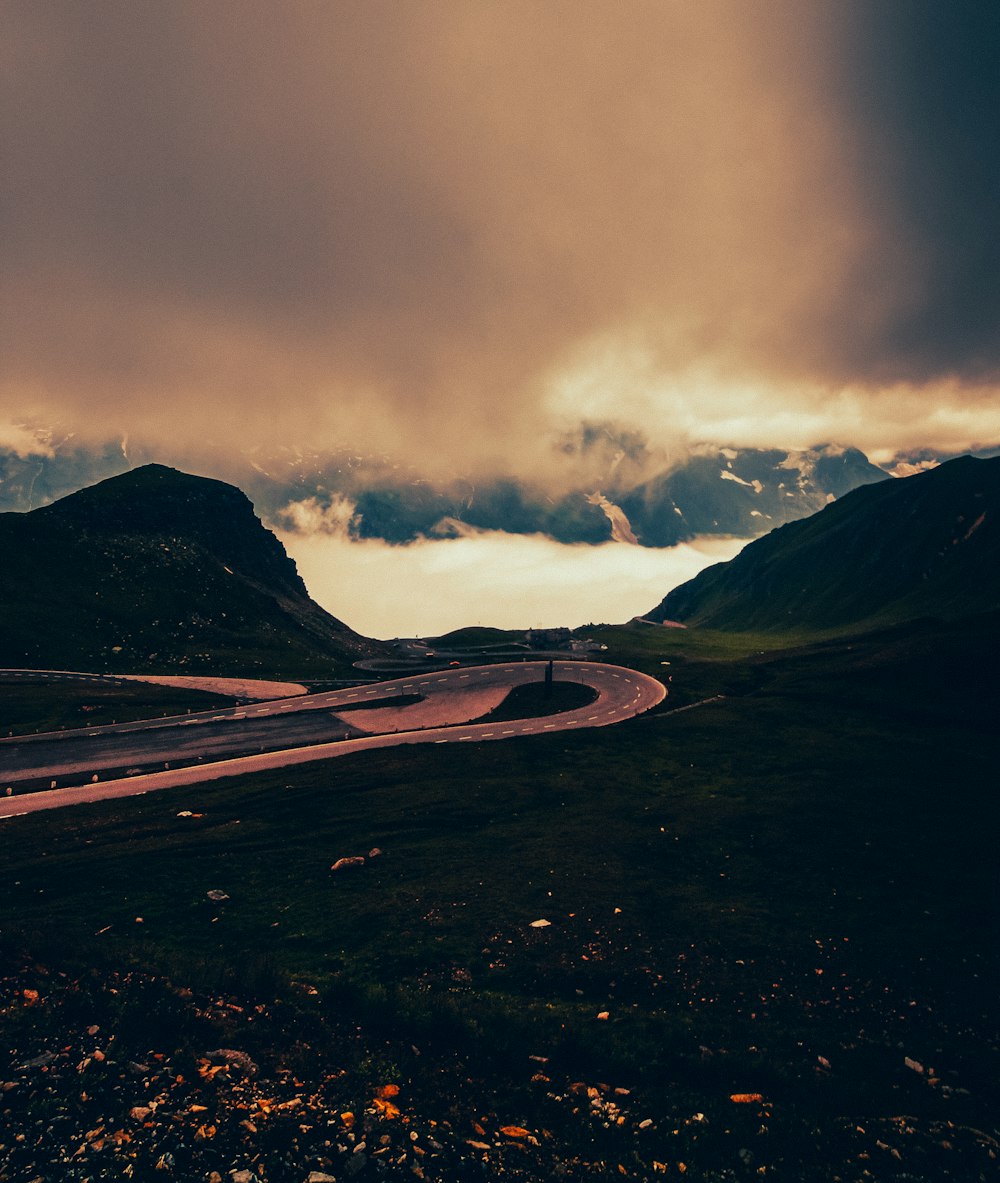 black asphalt road near mountain under cloudy sky during daytime