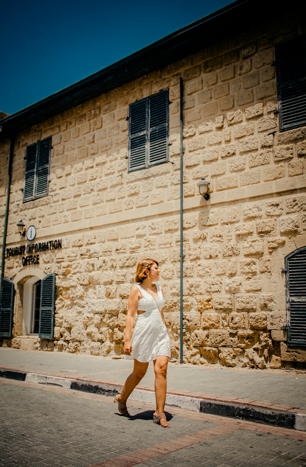 Donna in vestito bianco in piedi accanto al muro di mattoni marrone durante il giorno