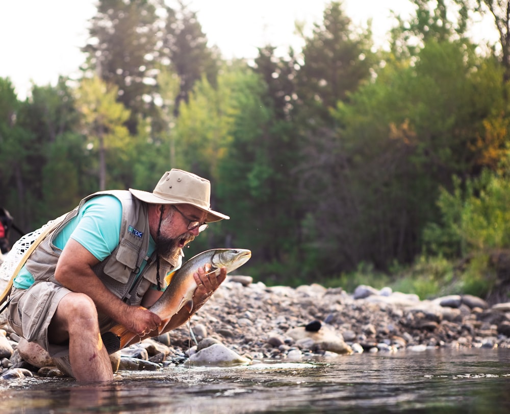 man in blue t-shirt and blue denim shorts sitting on rock in river during daytime