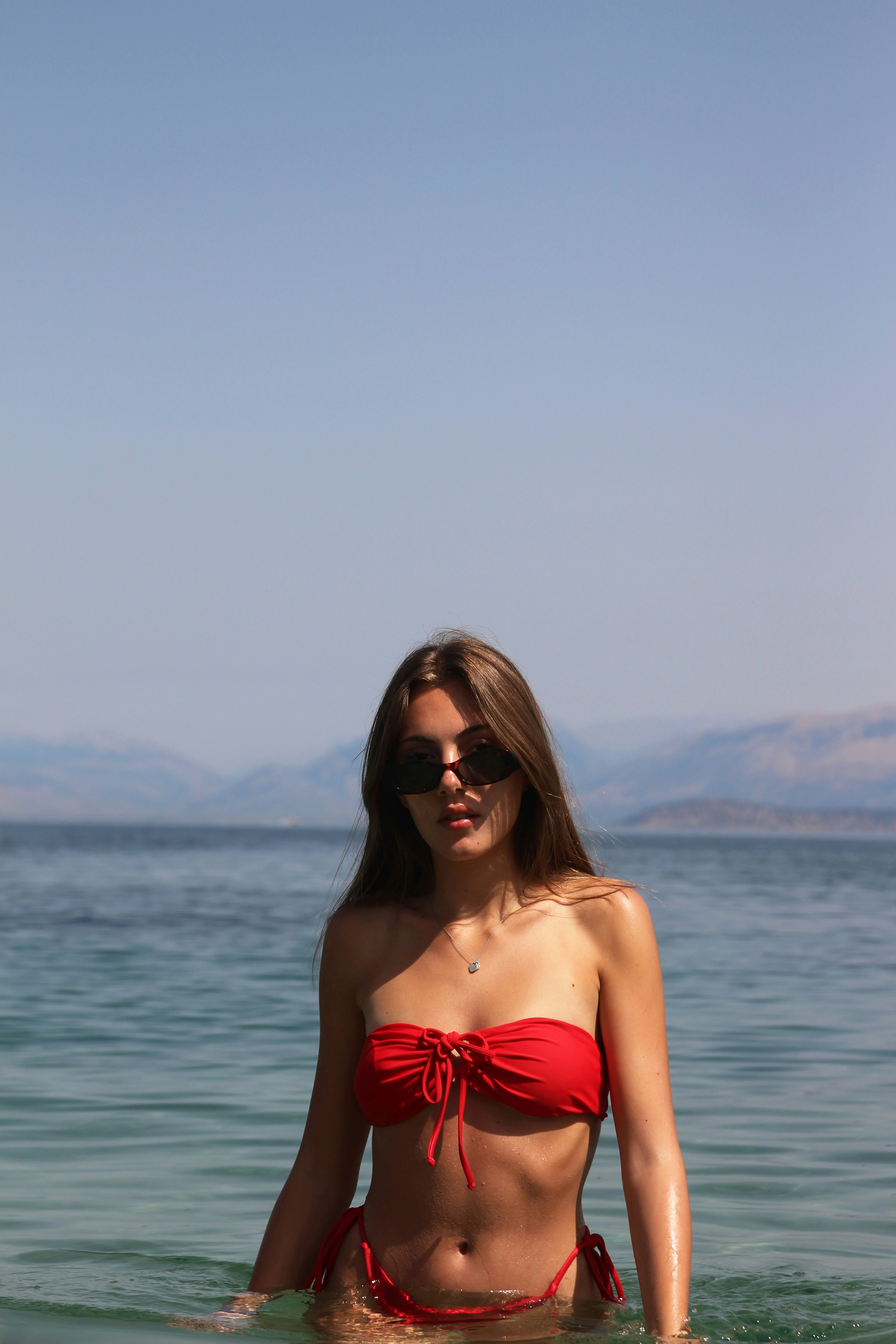 Mujer vestida de tubo rojo con gafas de sol negras de pie en la orilla del mar durante el día