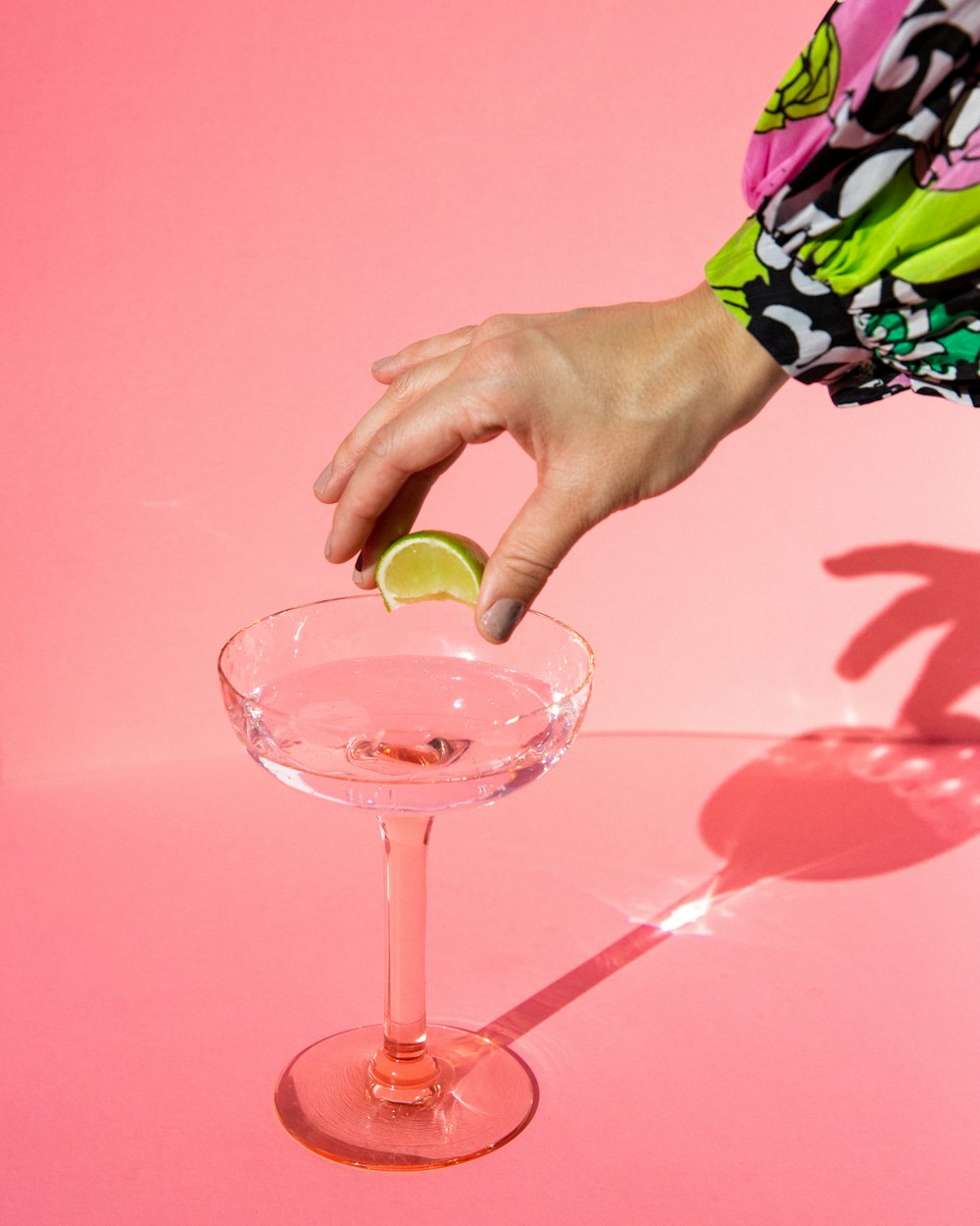 person holding clear wine glass with pink liquid