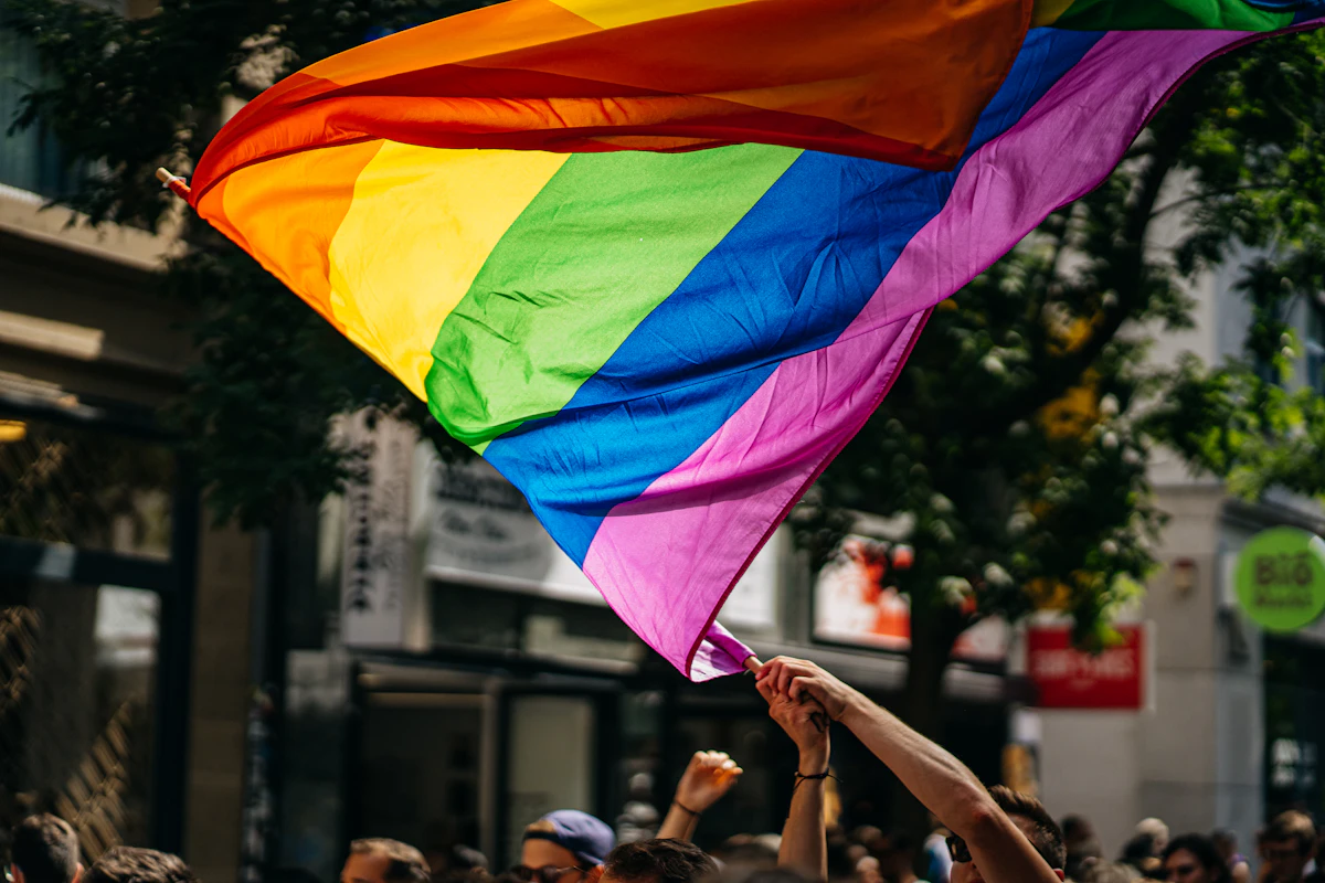 People holding Pride flags together in daylight, representing queer community and joyful connection