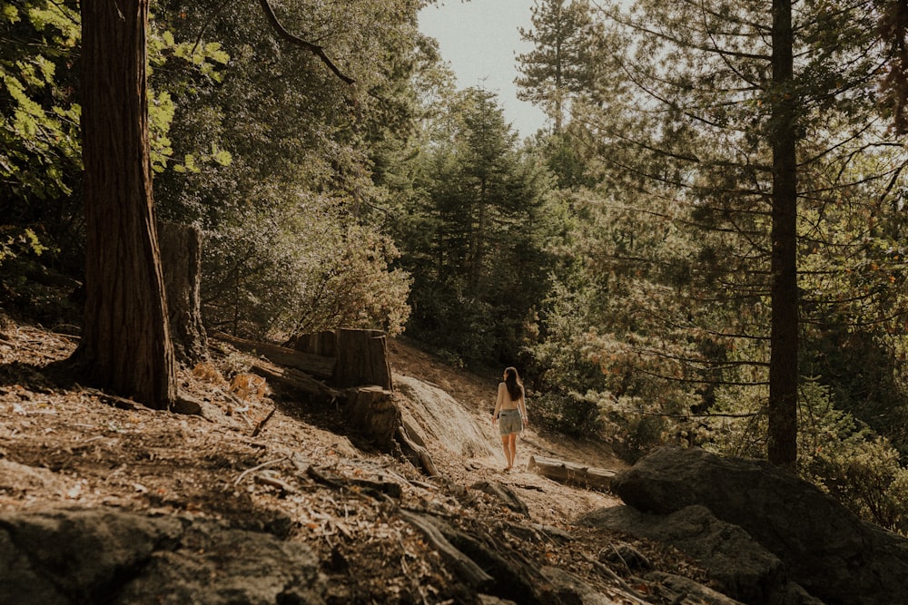 woman in black tank top and black pants standing on brown log in forest during daytime