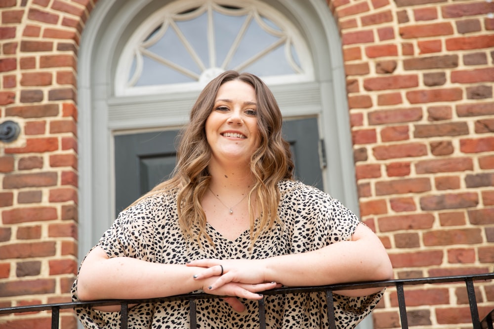 woman in black and white leopard print shirt standing near brown brick wall