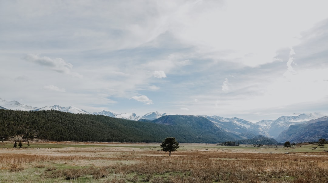 green grass field near mountain under white clouds during daytime