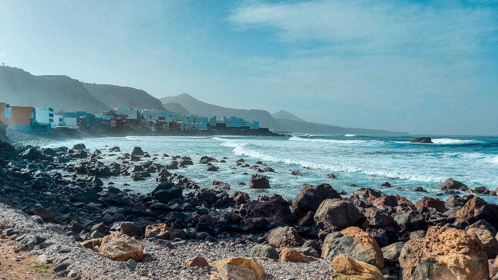 rocky shore with mountain in distance under blue sky with white clouds during daytime