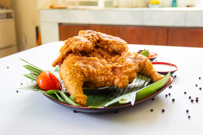 Close-up of crispy golden fried ayam pop served with sambal and fresh lime on a rustic plate