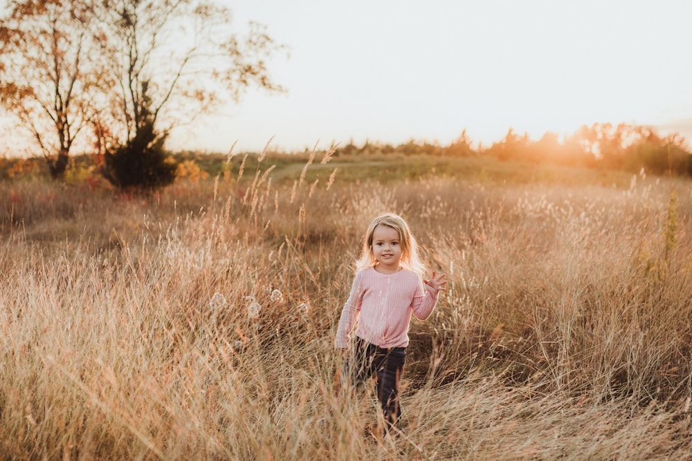 girl in pink long sleeve shirt standing on brown grass field during daytime