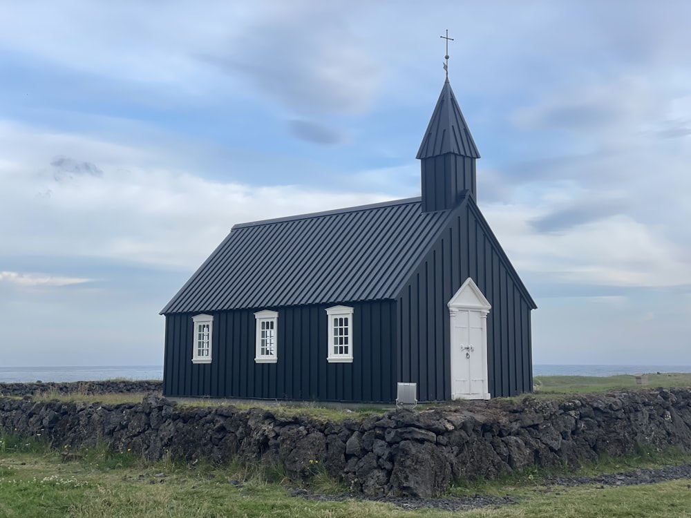 igreja de madeira preta e branca no campo de grama verde sob nuvens brancas e céu azul durante