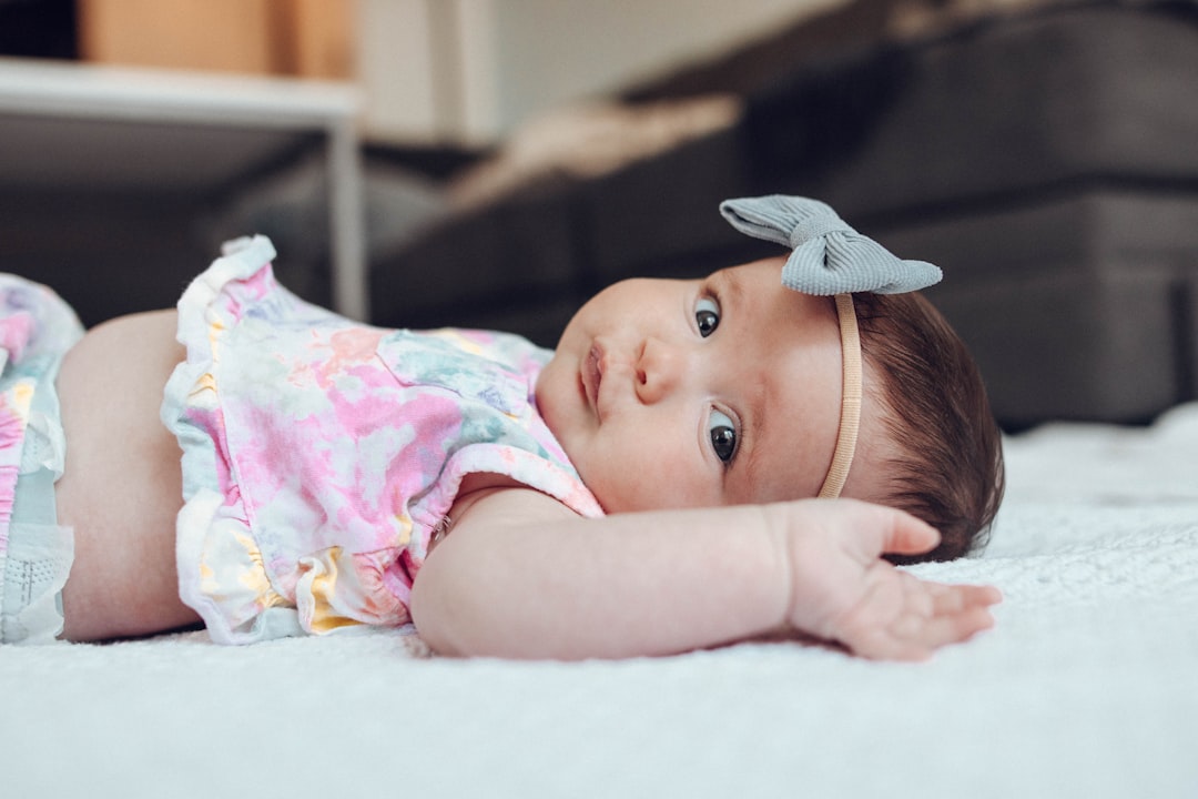 baby in white pink and green floral shirt lying on white textile