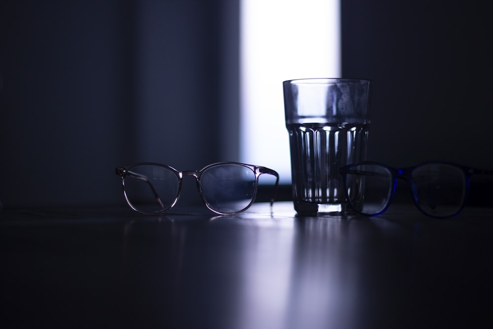 black framed eyeglasses beside clear drinking glass