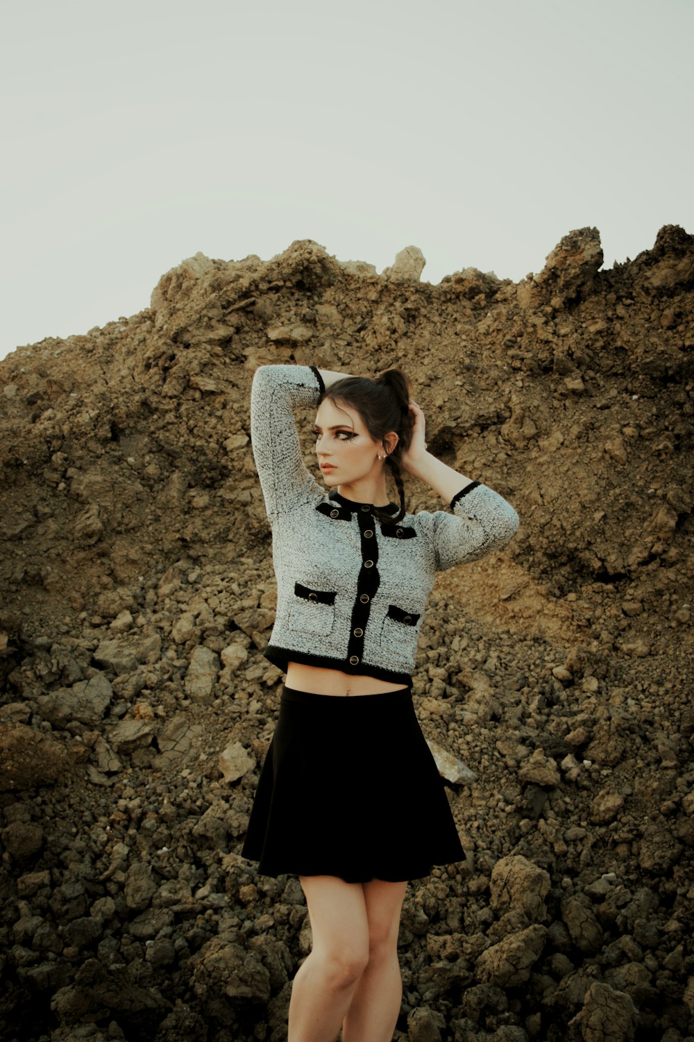 woman in gray knit sweater and black skirt standing on brown rock formation during daytime