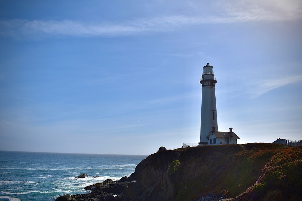 white and black lighthouse on brown rock formation near body of water during daytime