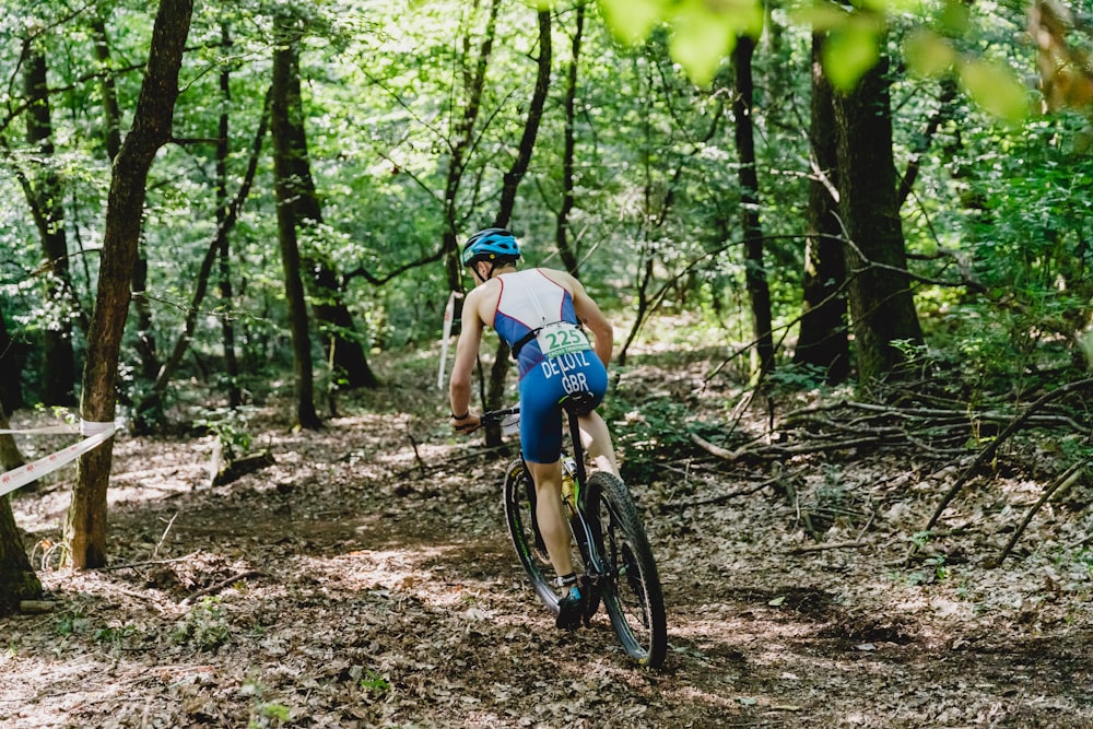 man in blue tank top and blue shorts riding bicycle in forest during daytime
