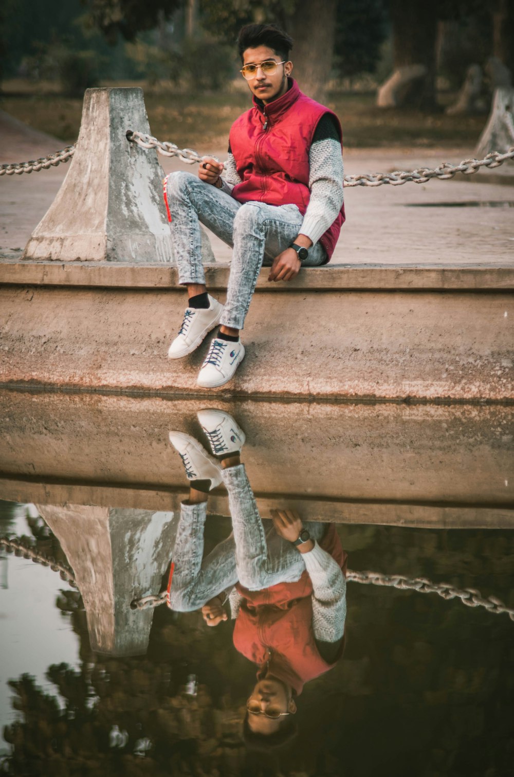 person in red jacket and blue denim jeans sitting on concrete bridge