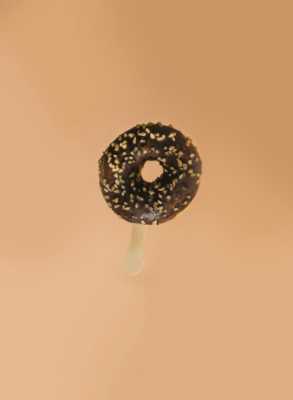 um donut de chocolate com polvilhos em uma vara
