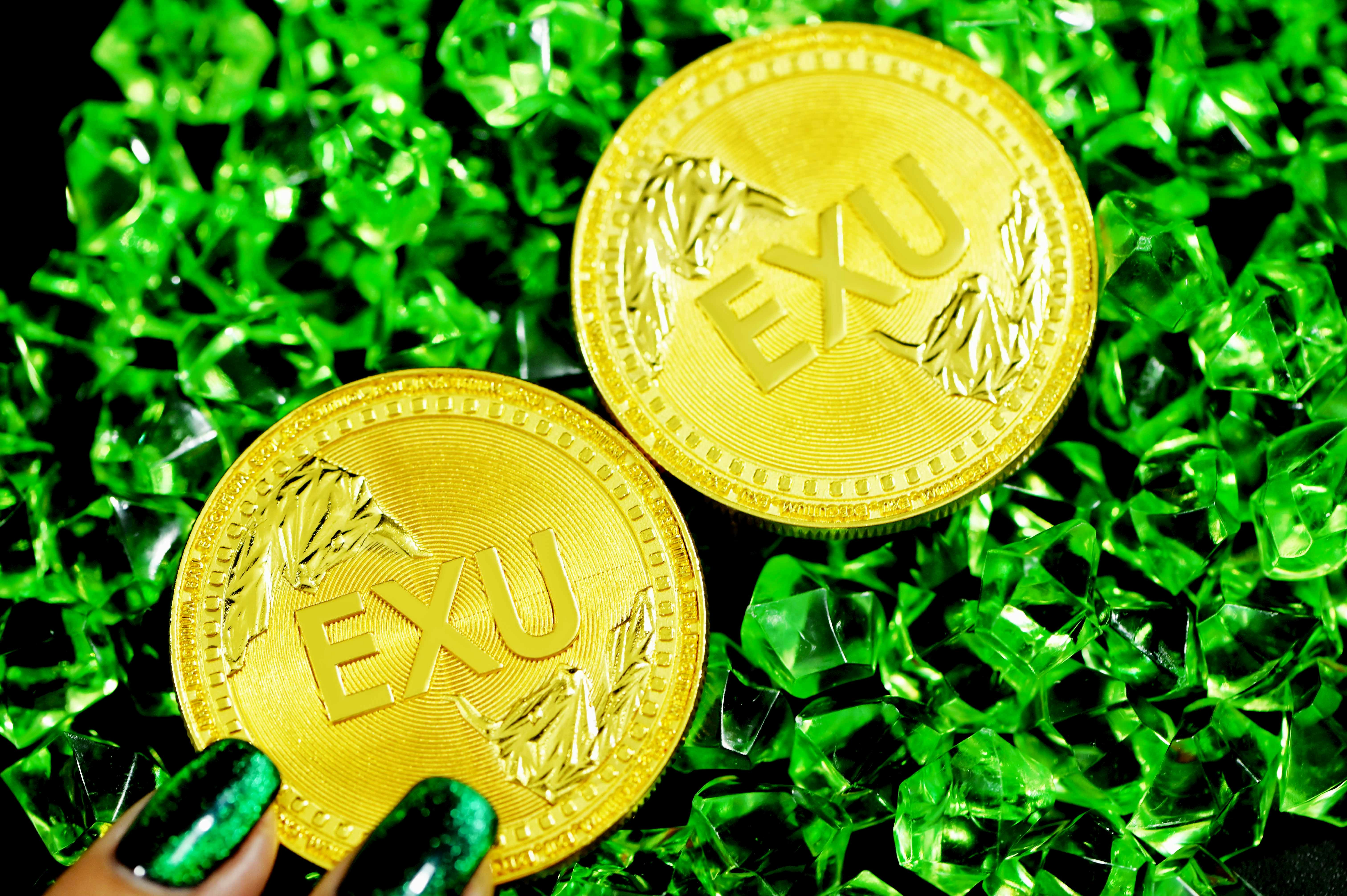 Two gold EXU coins on top of green crystals