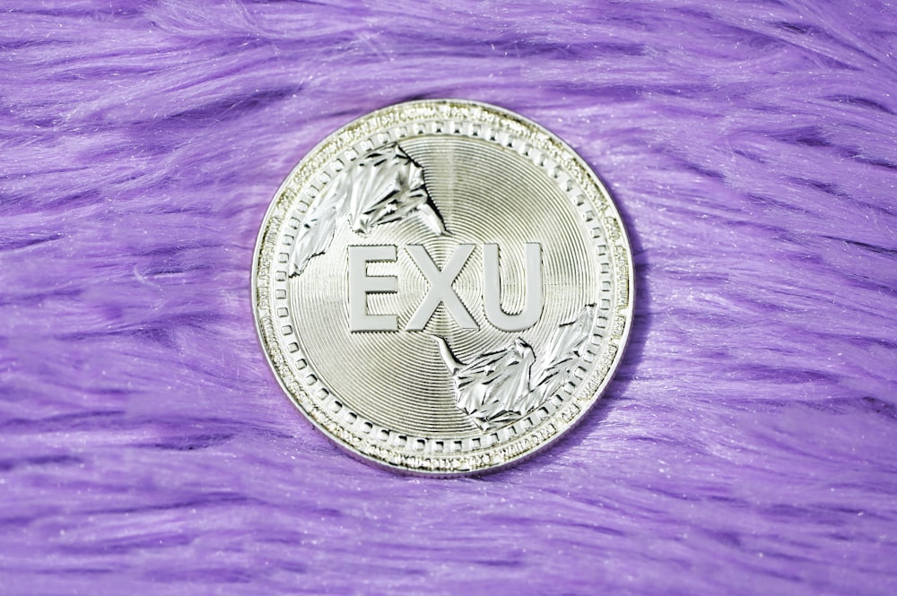 silver round coin on purple textile