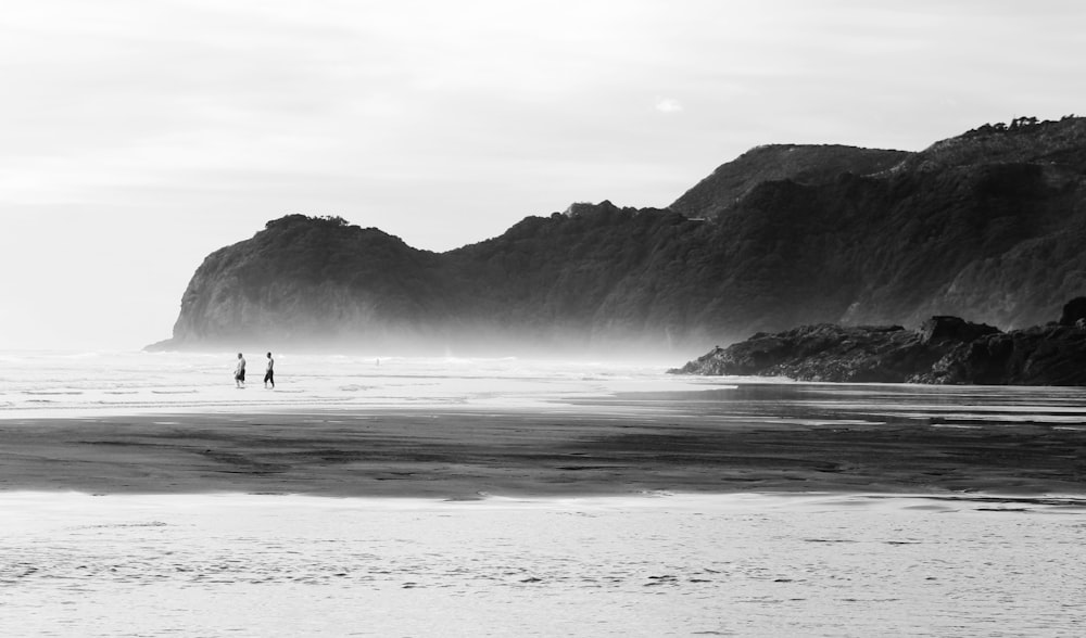 해변을 걷는 2명의 그레이스케일 사진