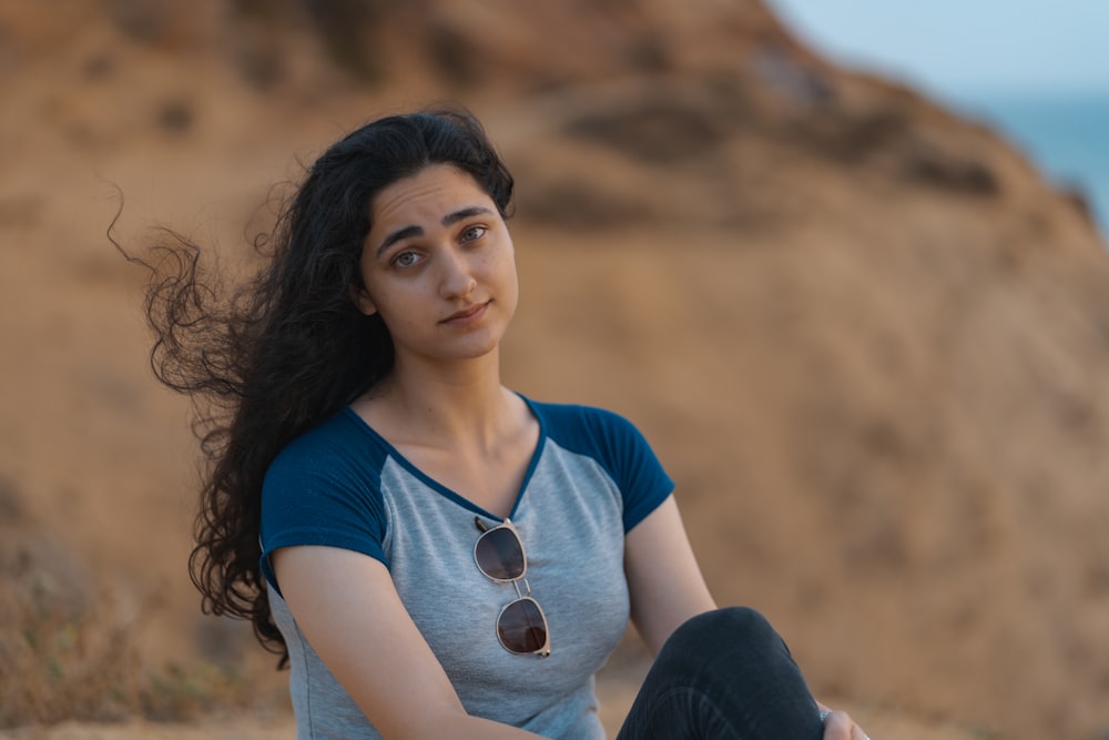 woman in blue scoop neck shirt and black pants sitting on brown field during daytime