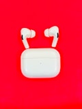 A pair of white wireless earbuds with a matching charging case is placed on a bright red background. The earbuds are positioned above the case, suggesting they are in use or being displayed. The stark contrast between the white earbuds and the vibrant red background gives the image a striking appearance.