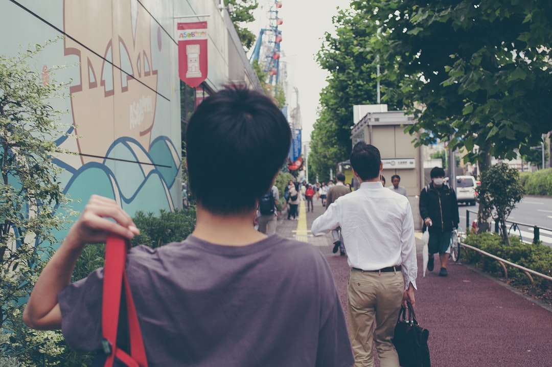 man in white crew neck t-shirt standing near people walking on street during daytime