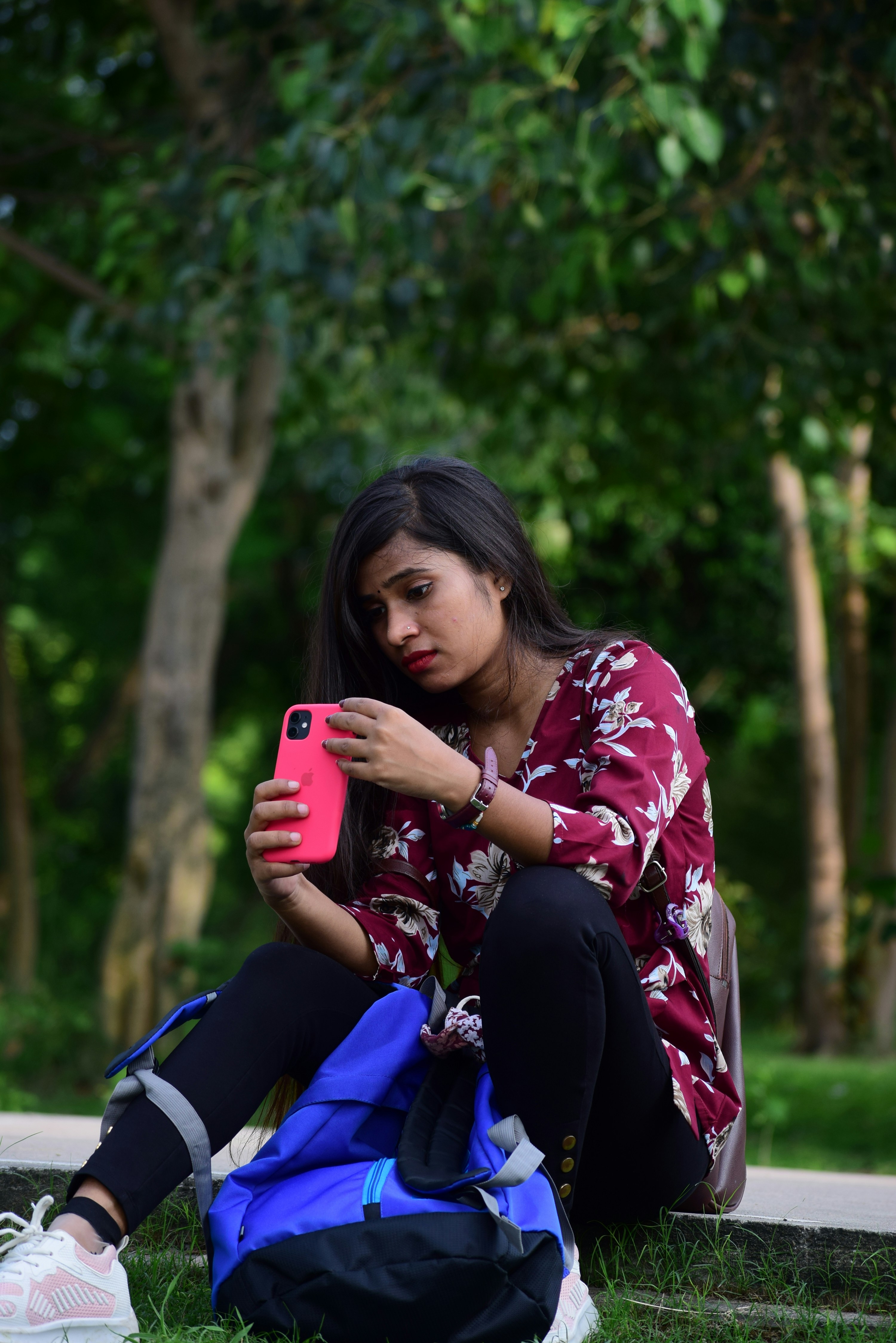 Wanita dengan kemeja lengan panjang bunga merah dan putih memegang smartphone merah muda