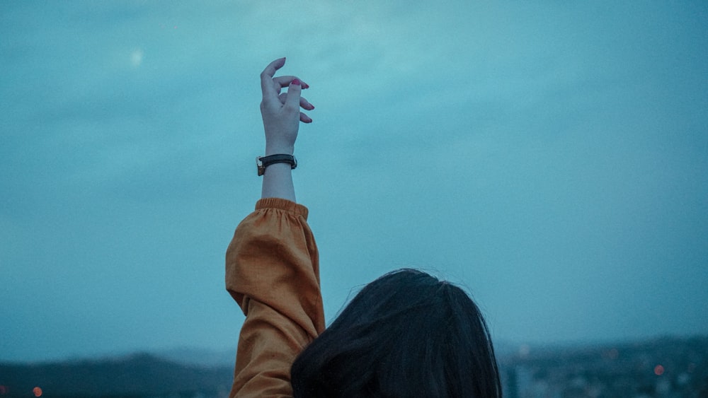 woman in brown jacket raising her left hand