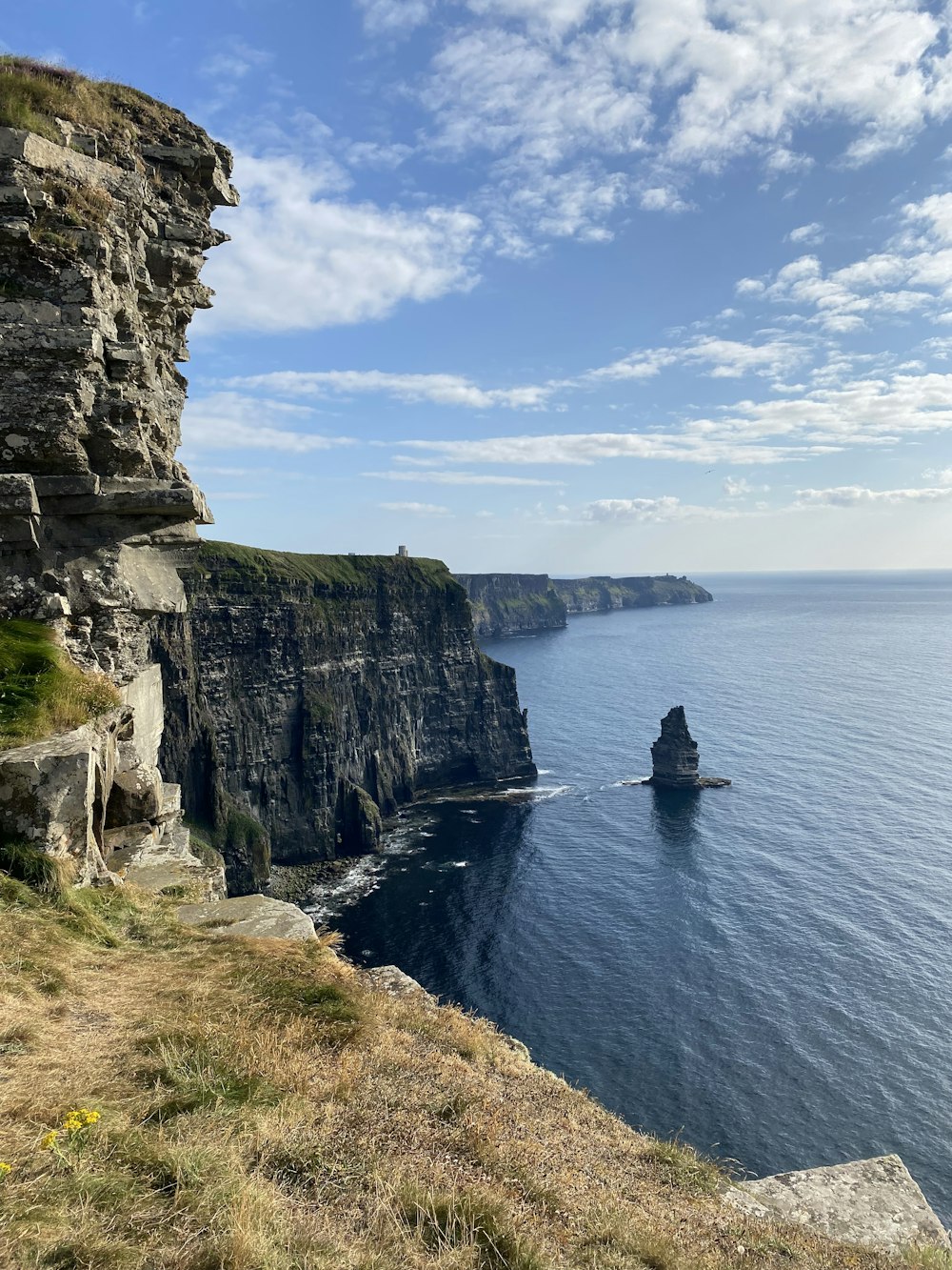 person in black jacket sitting on cliff by the sea during daytime