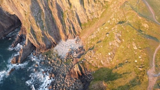 A dramatic coastline with waves crashing against cliffs, viewed from a drone hovering over the sea.