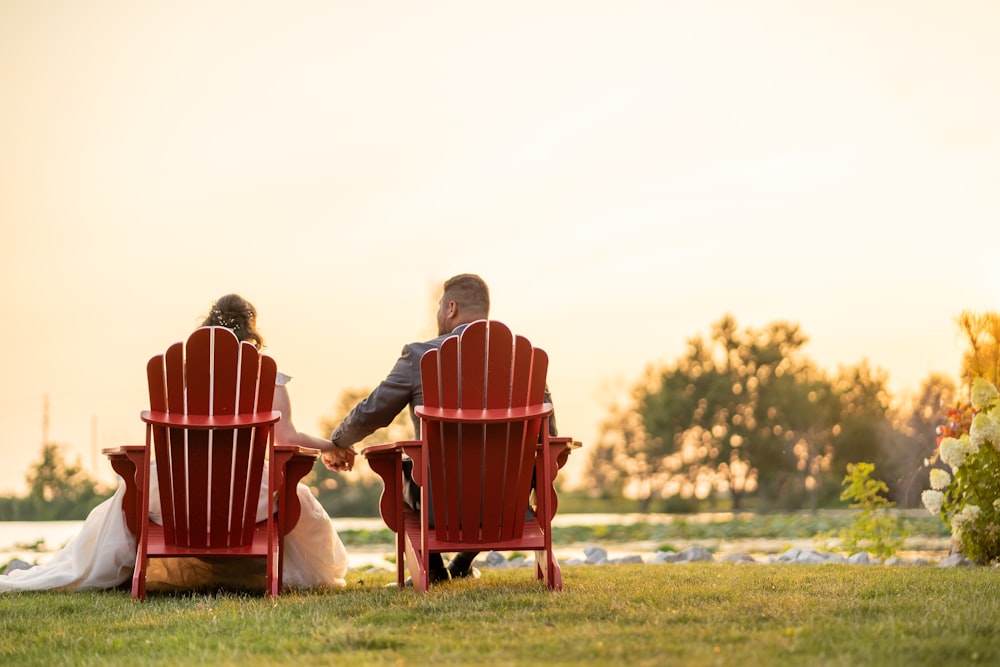 昼間、緑の芝生の上で赤い椅子に座る男女