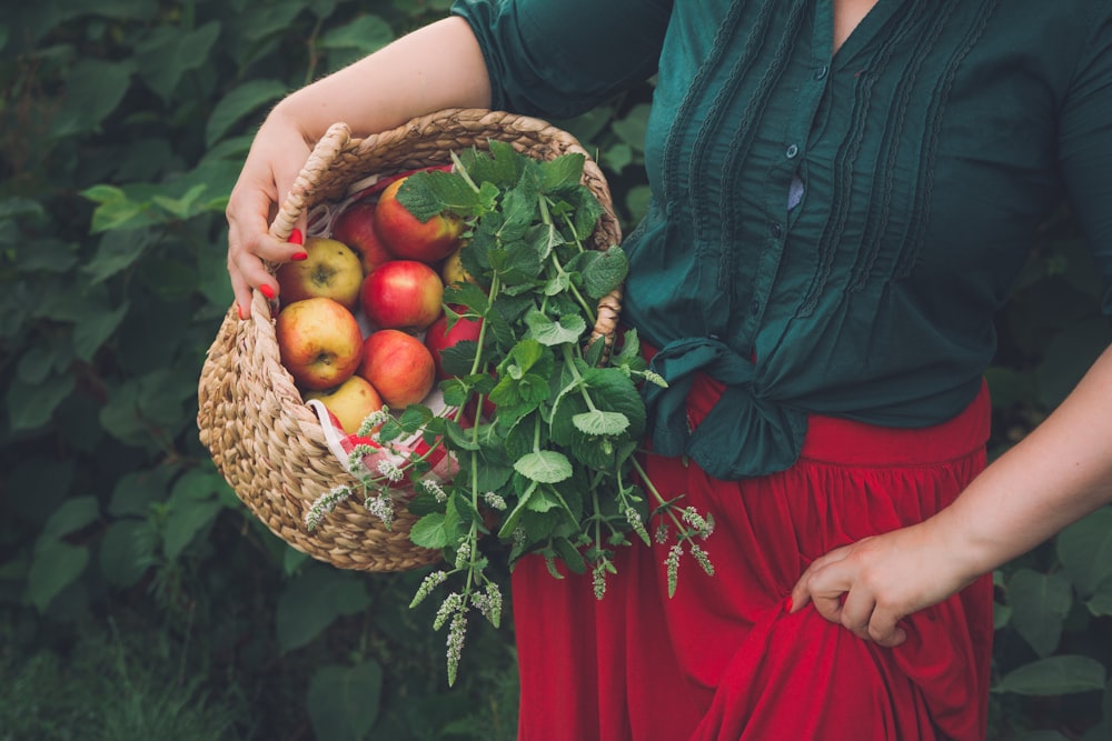 woman in red dress holding brown woven basket with red and yellow fruits