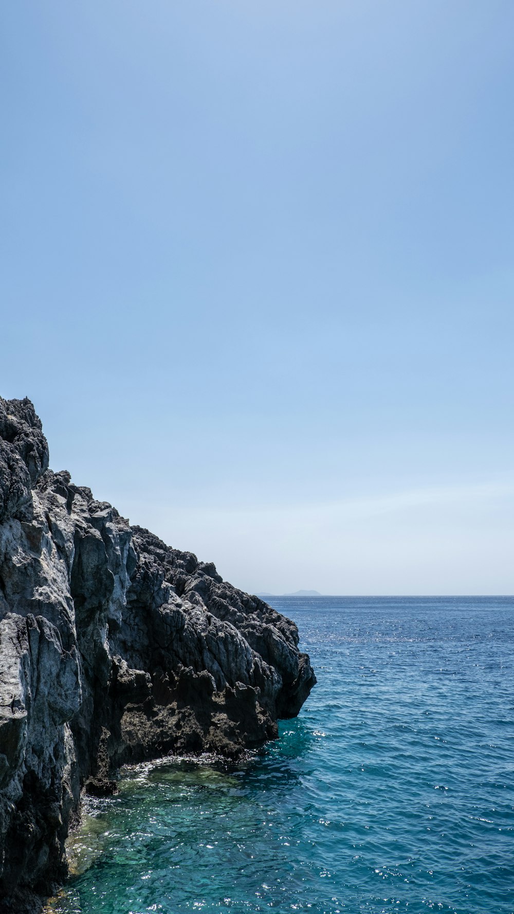 gray rocky mountain beside blue sea under blue sky during daytime