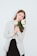 A person with long brown hair holds a bouquet of large white roses, wearing a striped blazer over a black dress. The background is plain light blue.